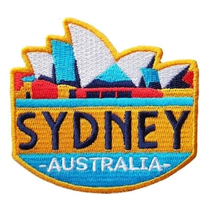 Puede incluir: Parche bordado con la Ópera de Sídney en blanco, azul y rojo, con un borde amarillo. La palabra "SYDNEY" está bordada en azul marino sobre "AUSTRALIA" en blanco, sobre un fondo azul.