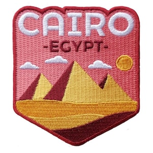 May include: Embroidered patch featuring the word "CAIRO" in white, above "-EGYPT-". The design includes pyramids, clouds, and a sun, all in shades of yellow, red, and pink. The patch has a red border.