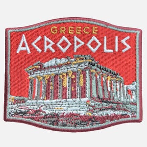 May include: Embroidered patch featuring the Acropolis in Greece. The patch has a red background with the word "GREECE" above "ACROPOLIS" in white. The Acropolis is depicted in detail with white, gray, and gold accents.