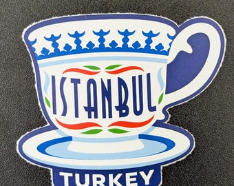 May include: A white and blue sticker in the shape of a teacup and saucer. The word "ISTANBUL" is written in blue letters across the cup. The word "TURKEY" is written in blue letters at the bottom.