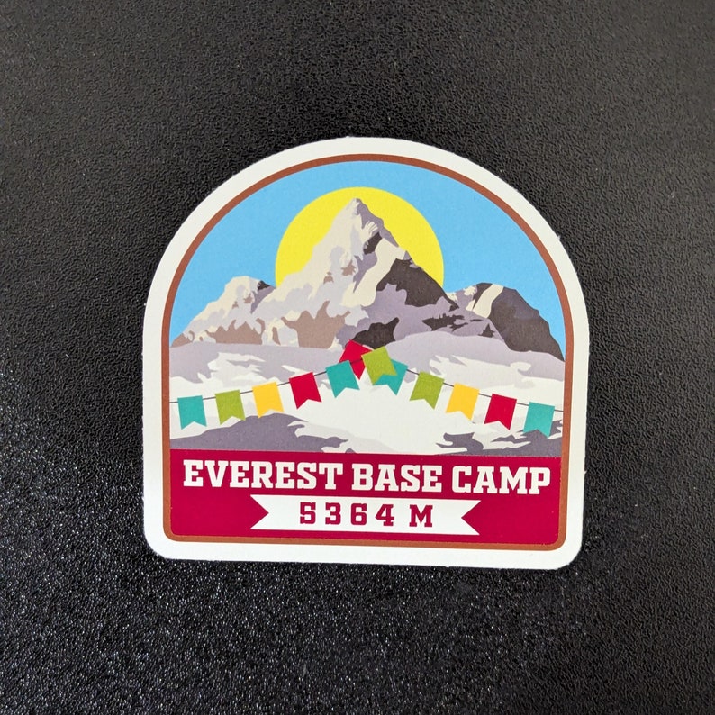 May include: A colorful sticker with a mountain scene and the text "Everest Base Camp 5364 M". The sticker features a mountain range with a yellow sun and colorful prayer flags.