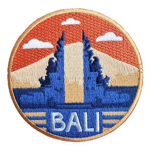 May include: Embroidered patch featuring a Bali landscape with blue temple gates, a beige mountain, and an orange sky with white clouds. The word "BALI" is embroidered in white at the bottom. The patch has a circular shape with a gold border.