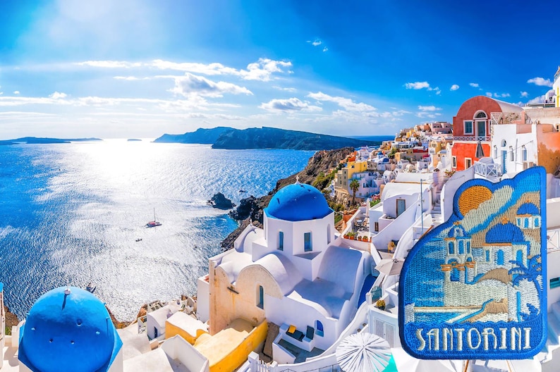 May include: A panoramic view of Santorini, Greece, with whitewashed buildings, blue-domed churches, and a bright blue sea. The image features a close-up of a souvenir patch with the word "Santorini" embroidered on it.