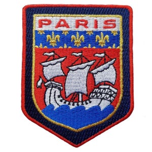 Könnte beinhalten: Gestickter Aufnäher mit einem Schilddesign. Das Wort "PARIS" steht oben, über einem roten Feld mit einem Segelschiff über blauen Wellen. Der Aufnäher ist rot, blau und gold umrandet.
