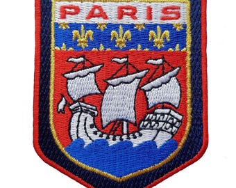 Puede incluir: Parche bordado con un diseño de escudo. La palabra "PARIS" está en la parte superior, sobre un campo rojo con un velero sobre olas azules. El parche está bordeado en rojo, azul y dorado.