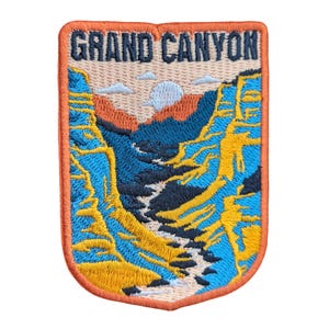 Könnte beinhalten: Gestickter Aufnäher mit einer Ansicht des Grand Canyon. Der Aufnäher hat einen orangefarbenen Rand und eine rechteckige Form. Das Design zeigt einen blauen Canyon, einen Fluss, eine Sonne und die weißen Worte "GRAND CANYON".