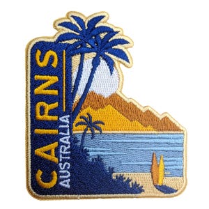 May include: Embroidered patch featuring a tropical beach scene with palm trees, ocean, and mountains. The patch has the text "CAIRNS AUSTRALIA" in gold and white lettering against a blue background, with a gold border.