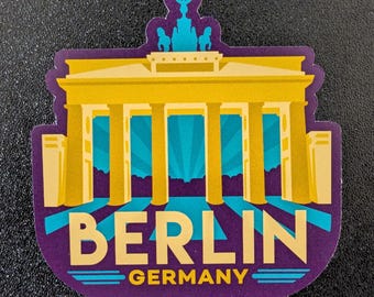 Könnte beinhalten: Ein Aufkleber mit dem Brandenburger Tor in Berlin, Deutschland. Das Design verwendet die Farben Gelb, Türkis und Lila. Das Wort "BERLIN" ist prominent dargestellt, mit "GERMANY" darunter.