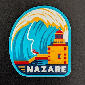 May include: A sticker with a design of a large wave with a surfer, a lighthouse, and the word "NAZARE". The wave is blue and white, the surfer is red, and the lighthouse is yellow and red. The sticker is a souvenir.