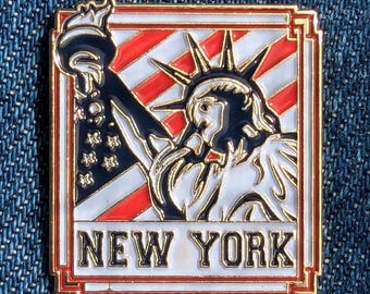 Może przedstawiać: Kwadratowa przypinka z wizerunkiem Statuy Wolności na tle czerwono-biało-niebieskich pasów. Przypinka ma złotą obwódkę i napis "NEW YORK" na dole. Statua jest biała z czarnymi i złotymi akcentami.