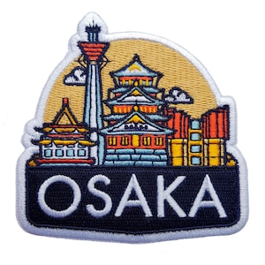 Könnte beinhalten: Gestickter Aufnäher mit Wahrzeichen von Osaka, darunter ein Turm und traditionelle Gebäude, vor einem beigen Hintergrund. Das Wort "OSAKA" ist in Weiß, blau umrandet, auf einem schwarzen Banner dargestellt.