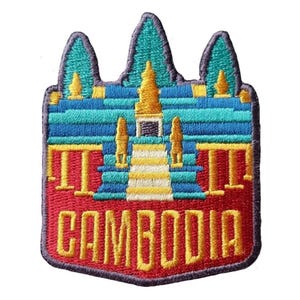 May include: Embroidered patch featuring a colorful depiction of a Cambodian temple. The patch has a red border and the word "CAMBODIA" in yellow. The temple design includes blue, yellow, and teal elements.