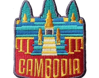 May include: Embroidered patch featuring a colorful depiction of a Cambodian temple. The patch has a red border and the word "CAMBODIA" in yellow. The temple design includes blue, yellow, and teal elements.