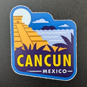 Puede incluir: Una pegatina con una colorida ilustración de Cancún, México. El diseño incluye una pirámide, el océano, palmeras y el texto "CANCUN MEXICO" en amarillo y blanco sobre un fondo azul y morado.