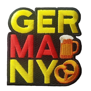 Puede incluir: Parche bordado con la palabra "GERMANY" en amarillo y rojo, con una jarra de cerveza y un pretzel. El parche tiene un borde negro y es probablemente para ropa o accesorios.