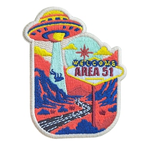 Pode incluir: Patch bordado com um OVNI sobre uma paisagem desértica, com o texto "WELCOME AREA 51" em estilo neon. O design apresenta uma estrada e montanhas em tons de vermelho, azul e amarelo. O patch tem formato retangular com borda branca.