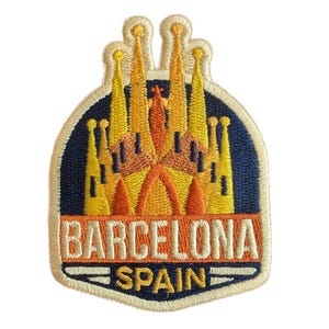 May include: Embroidered patch depicting the Sagrada Família in Barcelona, Spain. The patch has a navy blue background with the church in yellow and orange hues. The word "BARCELONA" is above "SPAIN" in a rectangular border.