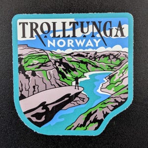 May include: A sticker featuring a scenic view of Trolltunga, Norway. The design includes a person standing on a cliff overlooking a lake and mountains. The sticker has a blue border and the text "TROLLTUNGA NORWAY".