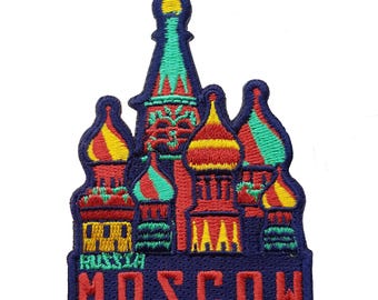 May include: Embroidered patch featuring a colorful depiction of Saint Basil's Cathedral in Moscow. The patch has a dark blue background with the word "MOSCOW" in red letters. The cathedral's domes are red, yellow, and green.