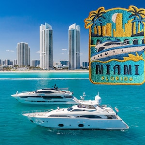 Op de afbeelding: Twee witte jachten liggen aangemeerd in turquoise water voor een skyline. De skyline omvat hoge gebouwen en een strand. Een blauw en geel geborduurd embleem met de tekst "Miami, Florida" bevindt zich in de rechterbovenhoek van de afbeelding.