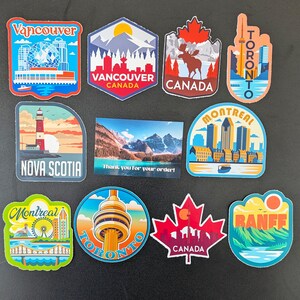May include: A selection of vibrant travel stickers showcasing Canadian destinations. The designs include the CN Tower, a maple leaf, and cityscapes of Vancouver, Toronto, and Montreal. A small card reads "Thank you for your order!"