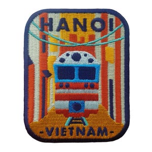 Peut inclure: Écusson brodé représentant un train à Hanoï, au Vietnam. Le design comprend le nom de la ville en haut et "Vietnam" en bas. L'écusson a une bordure bleue et un design de train coloré avec des accents orange, rouge et bleu.