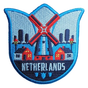 May include: A tulip-shaped embroidered patch featuring a central red and blue windmill, two red houses with yellow windows, and two street lamps against a light blue sky. The word NETHERLANDS is stitched in white at the bottom of the patch.