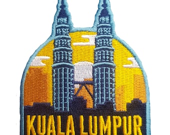 May include: Embroidered patch featuring the Petronas Twin Towers in Kuala Lumpur, Malaysia. The design includes the towers in blue, a yellow and orange sunset, and the city skyline. The text "KUALA LUMPUR" is embroidered in a bold, navy blue font.