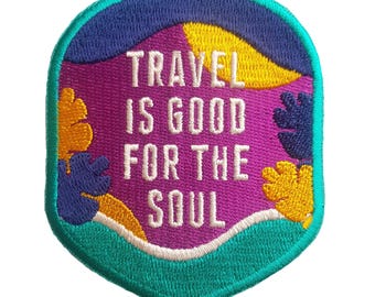 May include: Embroidered patch with the text "TRAVEL IS GOOD FOR THE SOUL". The patch has a purple background with yellow, blue, and teal accents. The border is teal and the text is white.