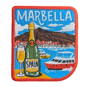 May include: Embroidered patch featuring the word "MARBELLA" above a scenic view. The design includes a champagne bottle, a glass of champagne, boats, and a mountain range. The word "SPAIN" is on the bottle. The patch has a red border.
