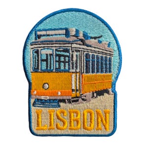 Könnte beinhalten: Gestickter Aufnäher mit einer gelb-orangenen Straßenbahn von Lissabon vor hellblauem Himmel. Der Aufnäher hat einen blauen Rand und das Wort "LISBON" in gelben Buchstaben.