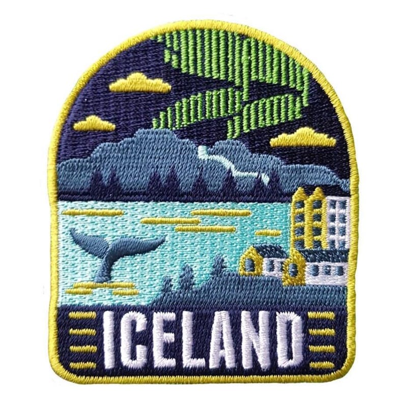 May include: Embroidered patch featuring an Icelandic landscape. The design includes a whale tail, mountains, buildings, and the text "ICELAND". The patch has a navy blue, teal, yellow, and green color scheme, with a yellow border and a depiction of the Northern Lights.