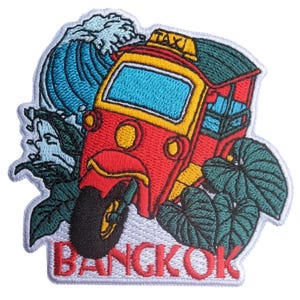 May include: Embroidered patch featuring a red, yellow, and blue tuk-tuk taxi with the word "BANGKOK" in red. The design includes a blue wave and green foliage, creating a travel-themed aesthetic.