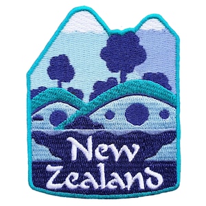 Peut inclure: Écusson brodé représentant un paysage de Nouvelle-Zélande. Le motif comprend des montagnes, des arbres et des collines dans des tons de bleu et de turquoise, avec le texte "New Zealand" en blanc.