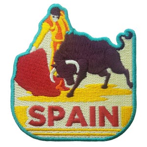 May include: Embroidered patch featuring a bullfight scene with a matador and a charging bull. The patch has a yellow, red, and purple color scheme with the word "SPAIN" in red letters at the bottom. The patch is outlined in teal.
