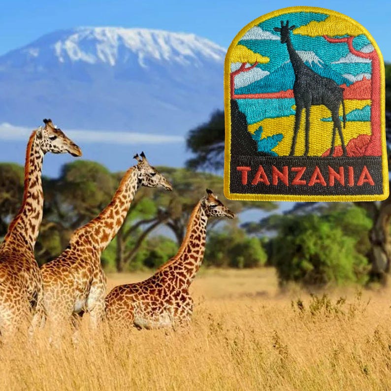 May include: An embroidered patch with a giraffe silhouette and the word "TANZANIA" against a colorful landscape. Three giraffes graze in a grassy field, with a mountain in the background.