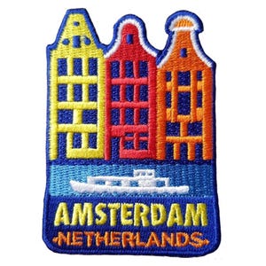 May include: Embroidered patch featuring three colorful canal houses in yellow, red, and orange, with a blue sky and water. The patch includes the text "AMSTERDAM NETHERLANDS" in yellow and orange.