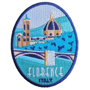May include: Embroidered patch featuring a stylized depiction of Florence, Italy. The design includes the Duomo, a tower, and a bridge, all in shades of blue, beige, and gold, with the city name and country below.