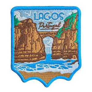 Puede incluir: Parche bordado con una vista de Lagos, Portugal. El diseño incluye un puente sobre una cascada, acantilados y el texto "LAGOS Portugal" en azul y blanco. El parche tiene un borde azul y un fondo marrón claro.