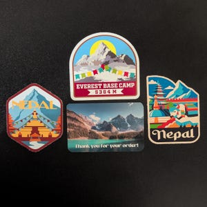 May include: Four colorful stickers featuring images of Nepal. The top sticker shows a mountain range with a yellow sun and the text "Everest Base Camp 5364 M". The sticker below it shows a mountain range with a lake and the text "Thank you for your order!" The sticker on the left shows a blue and red temple with the text "Nepal". The sticker on the right shows a colorful temple with the text "Nepal".