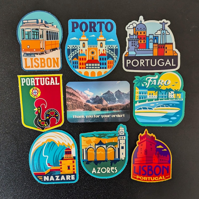 Może przedstawiać: Dziewięć kolorowych magnes&oacute;w przedstawiających r&oacute;żne zabytki i miasta w Portugalii, w tym Lizbonę, Porto, Faro i Azory. Magnesy są prostokątne i mają kolorystykę niebiesko-biało-czerwoną. Tekst "Dziękujemy za zam&oacute;wienie!" jest nadrukowany na osobnym magnesie.