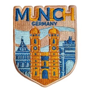 Puede incluir: Parche bordado con la palabra "MUNCH" en azul y dorado, y "GERMANY" debajo. El parche representa un paisaje urbano estilizado con edificios azules y dorados, incluyendo una iglesia con torres gemelas.