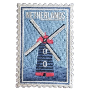 May include: Embroidered patch featuring a Dutch windmill design. The patch has a blue background with a windmill in shades of blue, red, and white. The word "NETHERLANDS" is embroidered at the top, within a postage stamp-style border.