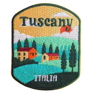 May include: Embroidered patch featuring a Tuscany landscape with the text "Tuscany" and "ITALIA". The design includes rolling green hills, cypress trees, and two buildings with orange roofs under a yellow sky with a red flag.