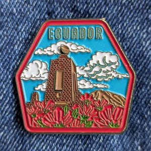 May include: A hexagonal pin featuring a colorful design of Ecuador. The pin has a red border, a blue sky background with white clouds, and a brown monument with red flowers in the foreground. The word "ECUADOR" is at the top.