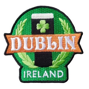 Könnte beinhalten: Gestickter Aufnäher mit einem Pint Stout, einem Kleeblatt und den Worten "DUBLIN" und "IRELAND". Das Design hat grüne, schwarze und orangefarbene Farben. Geeignet für Kleidung oder Accessoires.