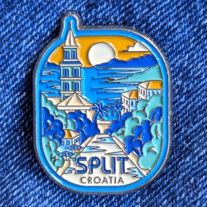Könnte beinhalten: Emaille-Anstecknadel mit einer Szene aus Split, Kroatien. Das Design zeigt einen Turm, das Meer, Palmen und Gebäude in Blau, Weiß, Gelb und Orange. Die Worte "SPLIT" und "CROATIA" sind unten auf der Nadel aufgedruckt.