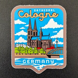 Puede incluir: Una pegatina cuadrada con un fondo de cielo azul y nubes blancas. La pegatina presenta una ilustración de la Catedral de Colonia en Alemania, con la palabra "Cologne" en una fuente estilizada. La palabra "Germany" está en la parte inferior.