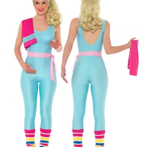 May include: A woman wearing a blue leotard with a pink belt and leg warmers. She is holding a pink towel in her right hand. The woman is wearing a blonde wig and has a bright smile.
