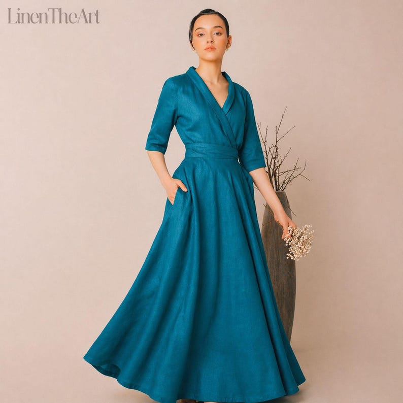 A woman wearing a long, blue dress with a wrap neckline and a high waist, posing with a bouquet of flowers in her hand.